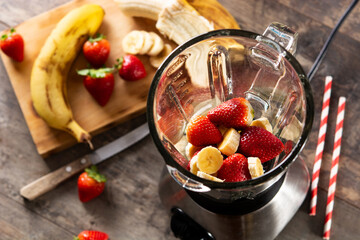 Preparing strawberry and banana smoothie in mixer on wooden table