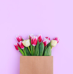 bouquet of colorful tulips in a paper bag on a pink background with space for text	
	
