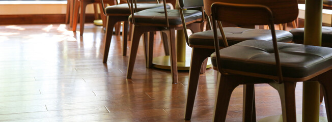 wooden floor and wood chairs with black cushion in a row at empty cafe restaurant with sunlight...