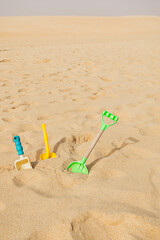 Fototapeta na wymiar Three children's plastic beach toys like shovel and rake on a yellow sand nature background with copy space. Travel with kid concept. Diy outdoor games. Sustainable fun. Eco-friendly toy.