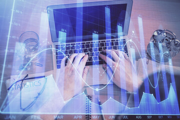 Double exposure of man's hands typing over laptop keyboard and forex chart hologram drawing. Top view. Financial markets concept.