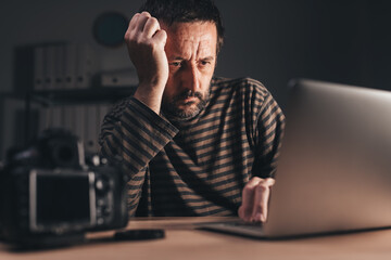 Photographer reviewing photos on laptop computer at his workplace