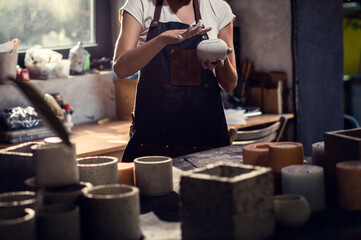 Craftswoman in apron working in her workshop making decorative concrete vase.