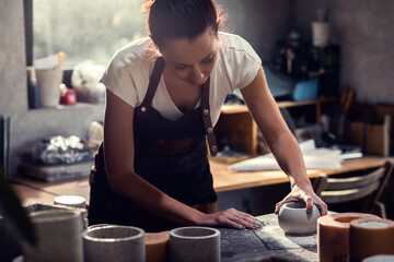 Craftswoman in apron working in her workshop making decorative concrete vase.