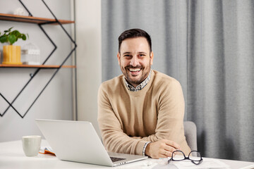 A happy freelancer sitting at his home office, working and smiling at the camera.