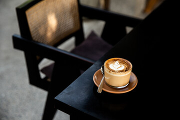 Glass of cappuccino with latte art on saucer and with spoon on the black table
