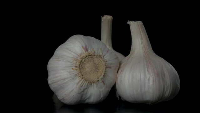 three heads of garlic rotate on a black background, close-up 