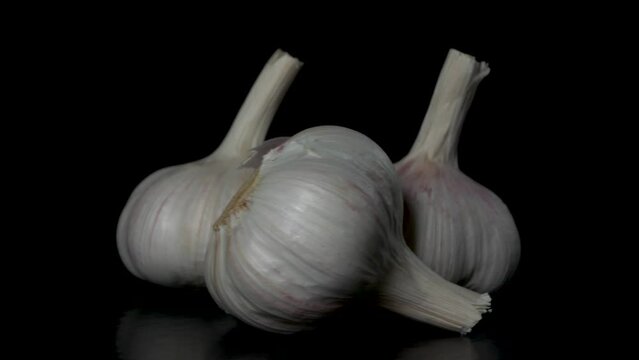 three heads of garlic rotate on a black background, close-up 
