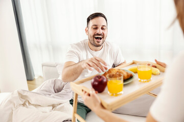 Fototapeta na wymiar A happy man having breakfast in the bed brought by his wife at their cozy home.