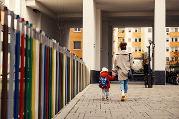 A nanny holding hands with little boy with a schoolbag and taking him to kindergarten. - obrazy, fototapety, plakaty