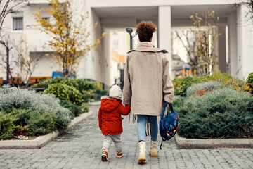 A mother holding hands with her little son and taking him home from kindergarten or daycare. - obrazy, fototapety, plakaty