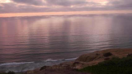 Dramatic cloudscape at sunset, reflection of pink sky, clouds. Torrey Pines scenic vista point, overlook viewpoint, ocean sea water waves from above. Steep cliff, rock or bluff, California coast, USA.
