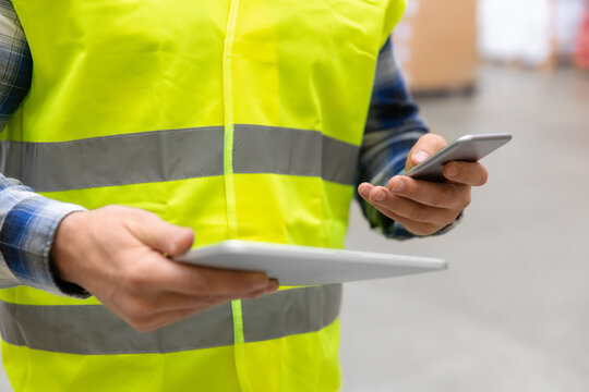 logistic business, technology, shipment and people concept - close up of man or manual worker with smartphone and tablet pc at warehouse