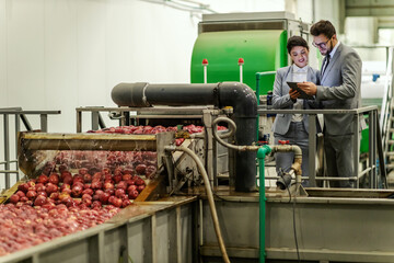 Businesspeople stand next to a washing machine for apples and check the effectiveness on a tablet.