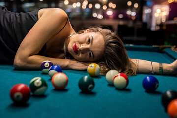 Beautiful woman in elegant black dress lying on the billiard table