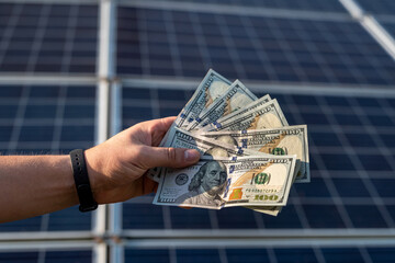 Human hands with dollar fan against solar panels. Saving energy concept