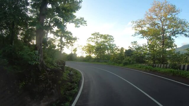 4K POV Hyper lapse of the dashcam of vehicle moving through the green forests of the Dang district on the way to Saputara in Gujarat, India. Car moving in forest with sun flare between trees in dawn. 