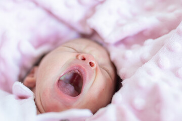 adorable newborn baby with closed eyes yawning with sleep in her crib wrapped in a pink blanket. - obrazy, fototapety, plakaty