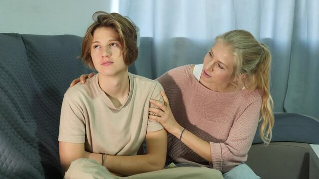 Upset teenager boy after quarrel with his mother in domestic interior, mother consoles son