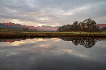 Beautiful morning light on Cumbrian mountains reflecting in calm river on a peaceful morning at The River Brathay in The Lake District, UK.