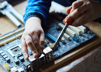 The hands of a teenager soldering chips on a computer board.