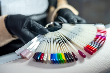 woman working in a nail salon offers a color of nail polish to one of her clients and smiles.