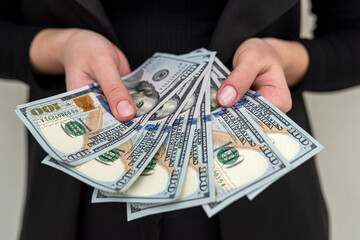 Beautiful young girl in a classic suit holding a large sum of dollars.