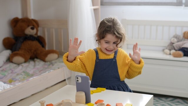 Funny little girl posing on smarthpone video doing dance sitting in room and laughing. Kids using phone app making selfie as a game