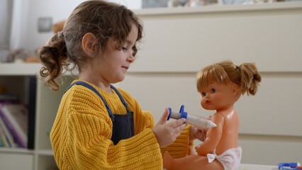 Adorable little girl makes an injection with a toy syringe to a doll in her bedroom, the concept of vaccination and child care. Medical games with dolls for toddlers and preschoolers