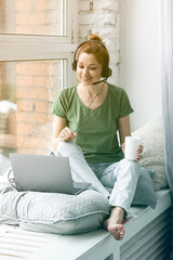 Beautiful young woman working remotely or studying at home at her laptop in the living room