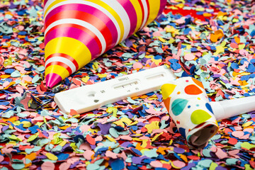 Fototapeta na wymiar Test kit for viral disease COVID-19 2019-nCoV laying in a bunch of confetti between a party hat and a party horn with a positive result. Fast test during carnival.