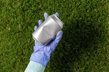 environment, volunteering and ecology concept - close up of hand in glove removing empty used tin can from grass