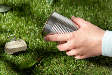 environment, volunteering and ecology concept - close up of hand removing empty used tin can from grass