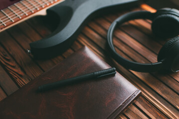Headphones, notebook and guitar on a wooden table. Musical theme.