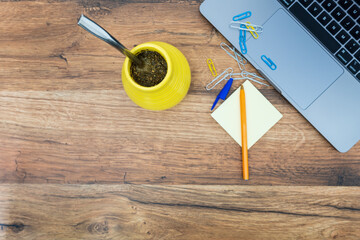 Widok z góry laptopa z argentyńskim yerba matę na drewnianym stole biurkowym. Obszar roboczy z laptopem, artykułami biurowymi, długopisem i yerba mate na tle drewna. Tło dla tekstu i projektu.