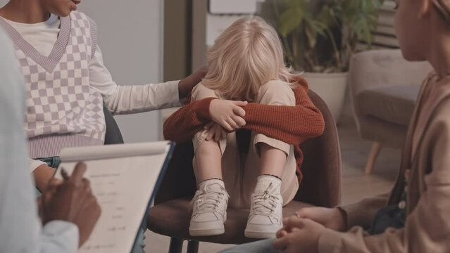 Slowmo shot of little Caucasian boy crying at group therapy session, while two diverse girls and African-American therapist comforting him