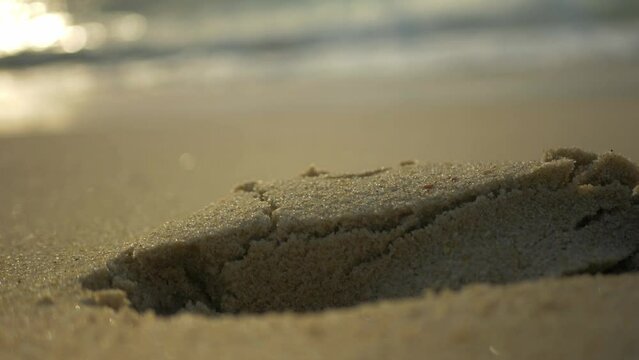 Close up of a foot walking on the sand next to the blue amazing ocean, leaving a hole. Amazing cloes up view of the sand in the beach and clear water.