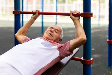 Obraz premium Open air gym. Street training on the municipal sports equipment. Elderly man pumps the press in city park