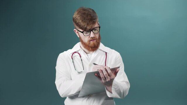 A young doctor in a white gown is writing something down on a tablet keeping in his hands