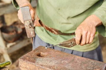 The hands of a blacksmith who forges a metal nail on an anvil. Ancient professions.