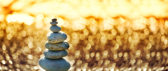 Pyramid of sea pebbles and sparkling sunny bokeh   in warm sunlight. Banner. . Artistic photo.

