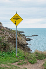 Ein gelbes Schild, das vor steilen Klippen warnt