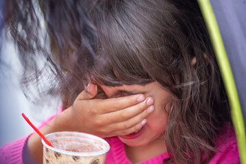 Crying baby girl on the stroller eating a cup of Ice Cream.