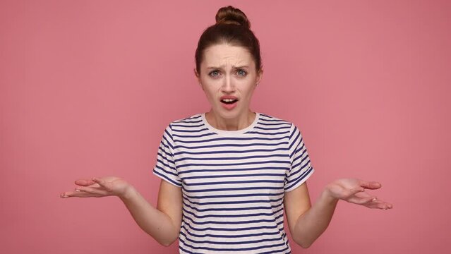 Irritated indignant woman, raising hands in anger and shouting why how, what do you want, quarreling, looking at camera, wearing striped T-shirt. Indoor studio shot isolated on pink background.