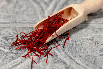 Closeup macro saffron on wooden shovel fine strands for traditional cuisine on blue grey tile table