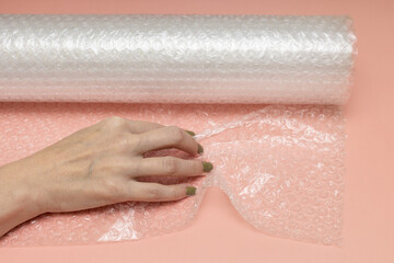 female hand crumples bubble wrap on a pink background