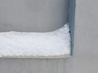 Snow layer stuck on concrete indent in gray cold wall