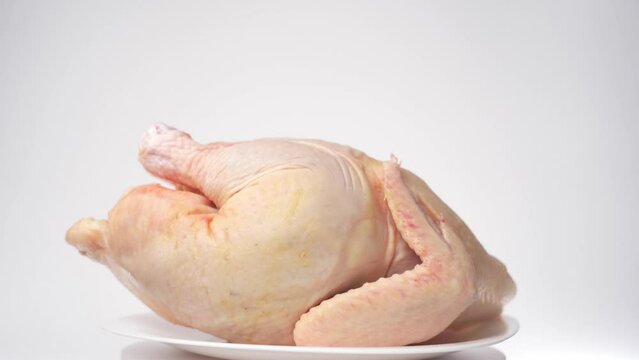 Chilled carcass of homemade chicken rotates on a white background, front view