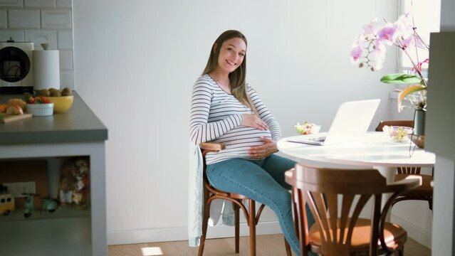 Pregnant woman sitting at table at home looking at camera.