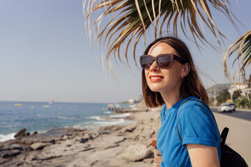 A woman in a blue t shirt and brown sunglasses enjoy the view of the sea with a palm tree in background